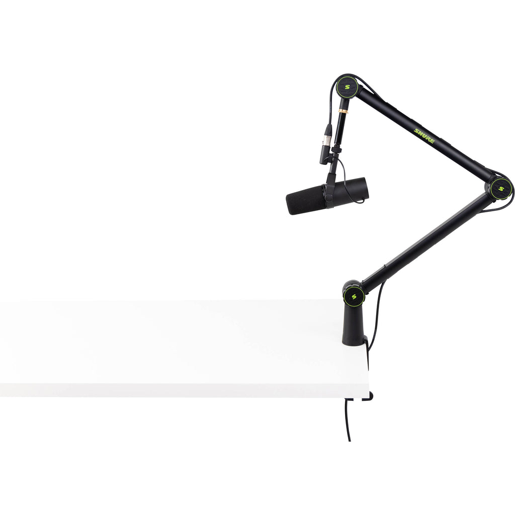 Shure SH-BROADCAST1 broadcast microphone arm mounted on a desk, adjustable arm with sleek black finish for professional audio setups.