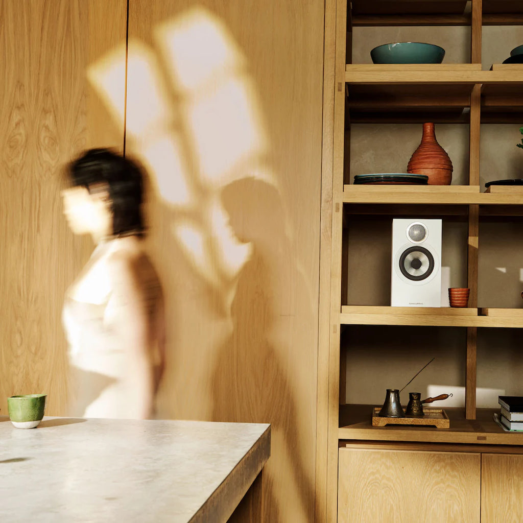 Bowers & Wilkins 607 S3 passive bookshelf speakers in white, shown in a lifestyle setting with a modern home interior.
