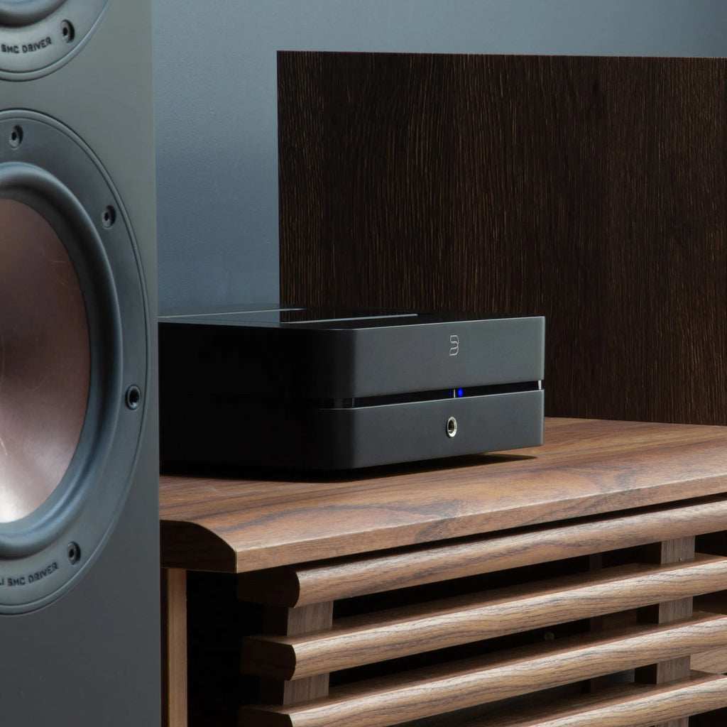 Bluesound Powernode 2025 music streamer in black, shown with DALI Opticon 6 MK2 speakers, close-up low right angle.