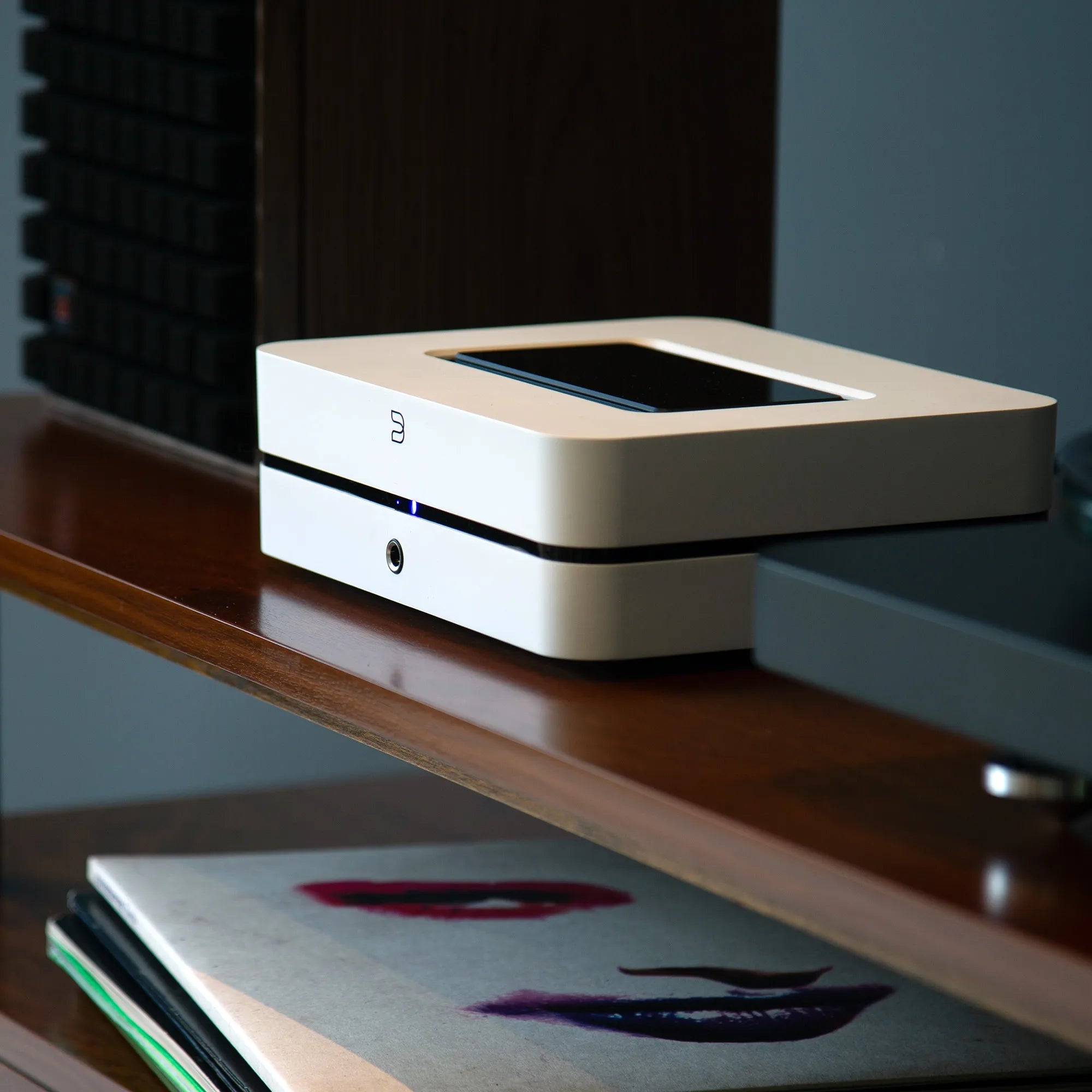 Bluesound Powernode 2025 music streamer in white with a turntable, showcasing compact design and audio equipment setup.