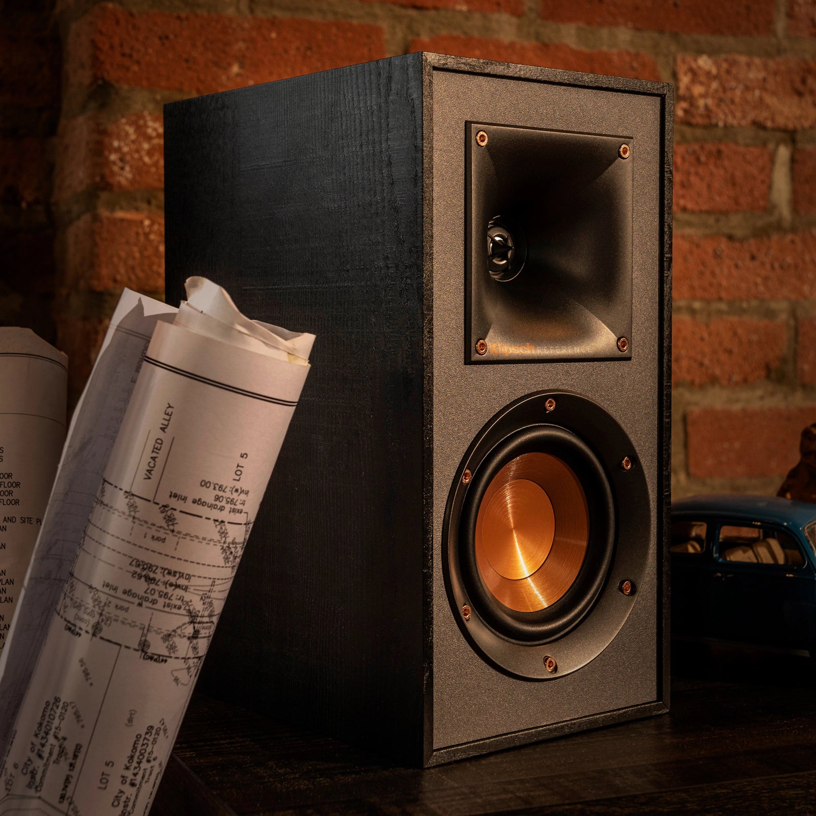 Klipsch R-41PM active bookshelf speakers with wood finish and front ports, positioned on a modern entertainment stand.