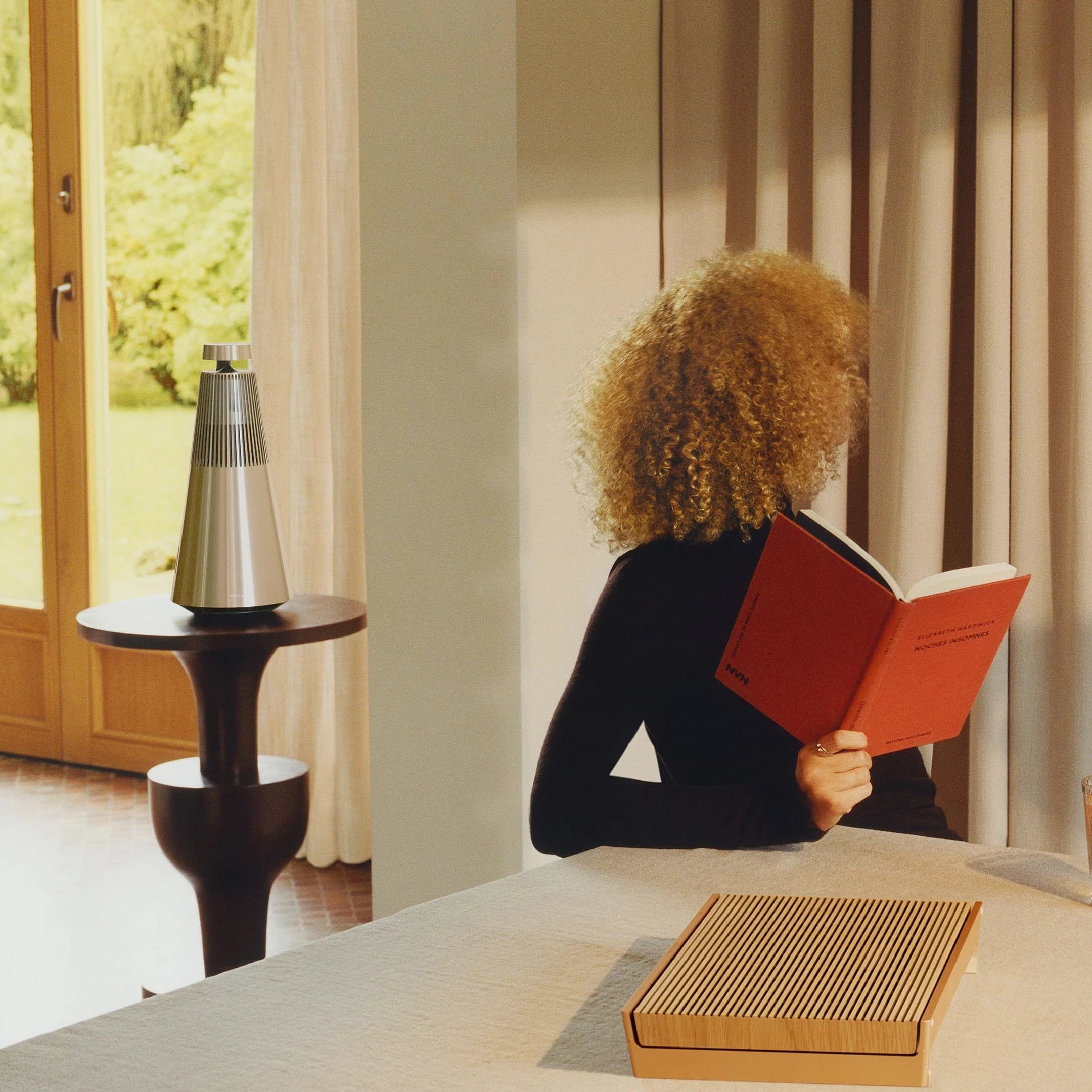 Bang & Olufsen Beosound 2 3rd Gen wireless speaker in a stylish living room setting showing its sleek cylindrical design