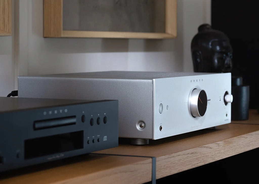 Onkyo Icon A-50 silver stereo amplifier beside Klipsch bookshelf speaker with wall art in the background.