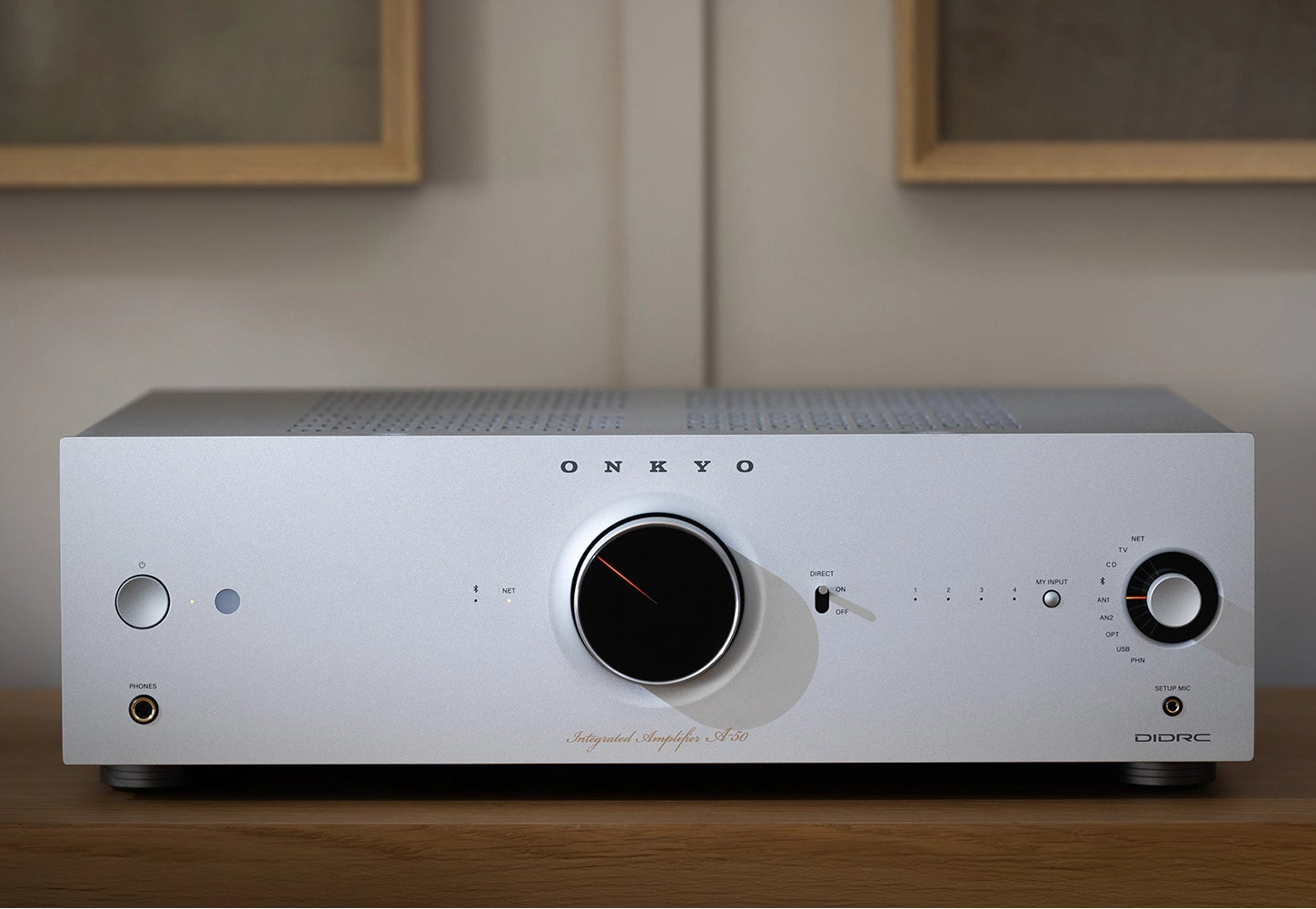 Close-up of the silver Onkyo Icon A-50 stereo amplifier on a modern cabinet, showcasing its sleek design and control knobs.