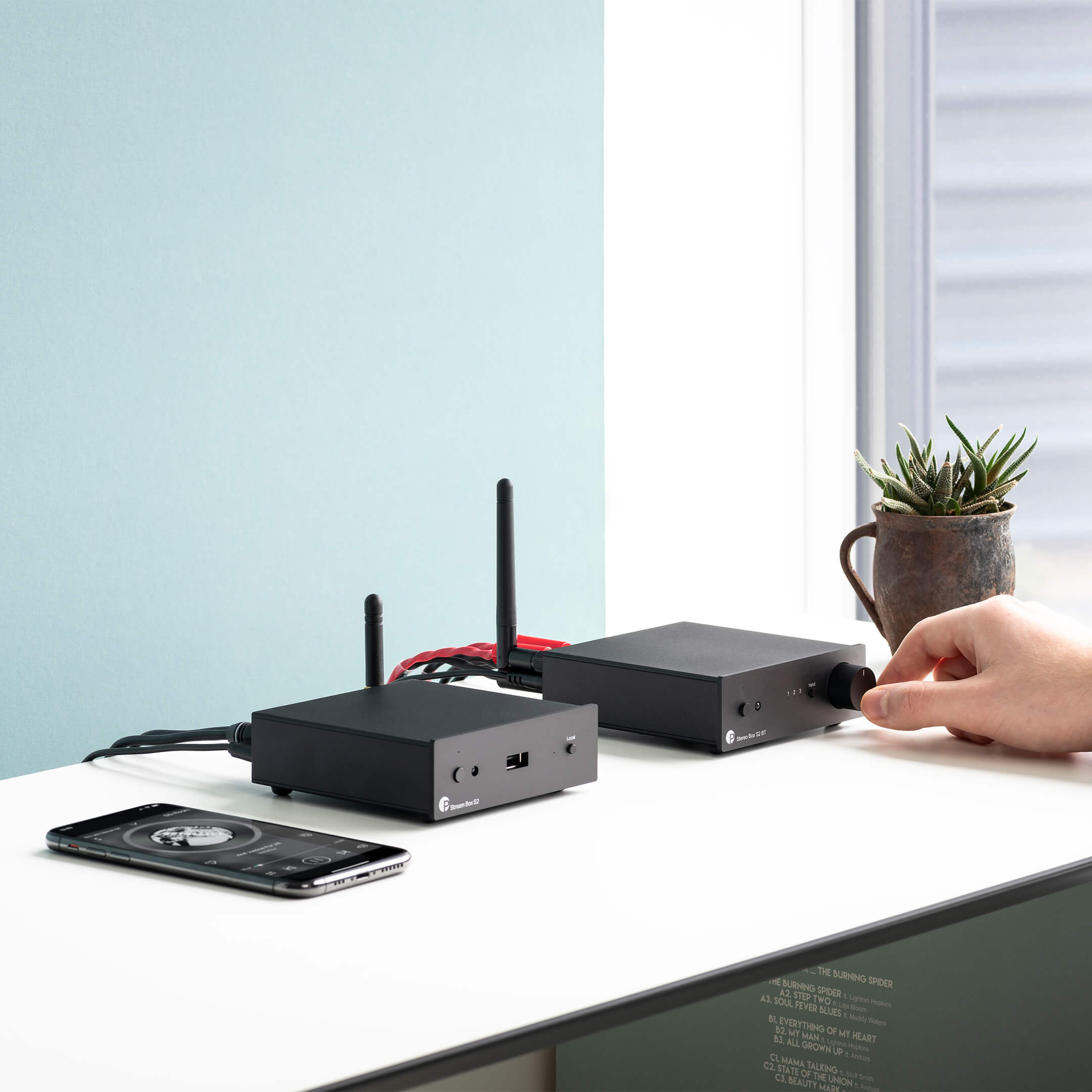 Pro-Ject Stream Box S2 music streamer in black, shown connected to audio equipment in a modern home entertainment setup.