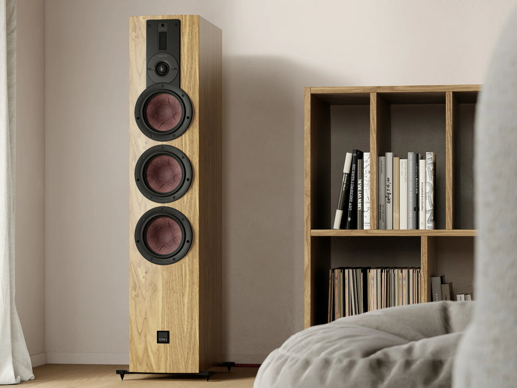 DALI Rubikore 8 passive floorstanding speakers shown in a modern living room setup with sleek wood finish and fabric grilles.