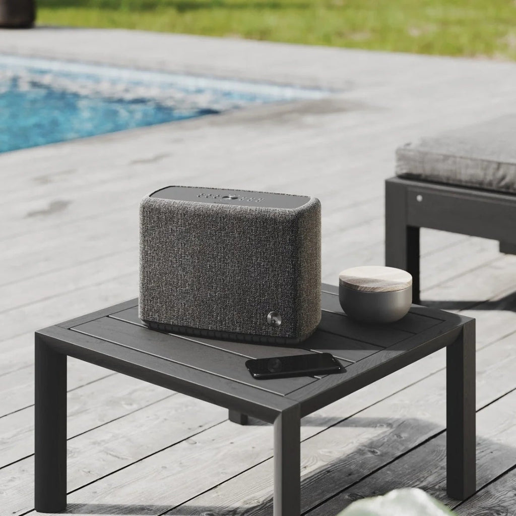 Audio Pro A15 portable speaker shown outdoors with rugged design, matte finish, and control buttons on top.