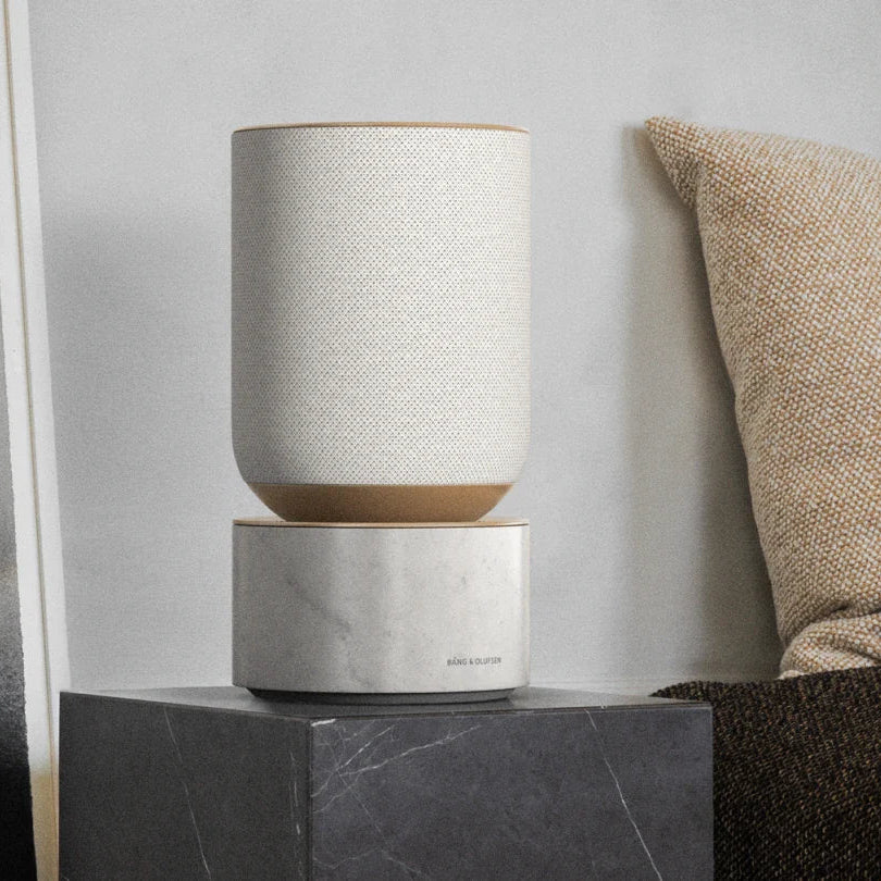 Bang & Olufsen Beosound Balance wireless speaker in a sleek, modern design with a fabric cover and wooden base.