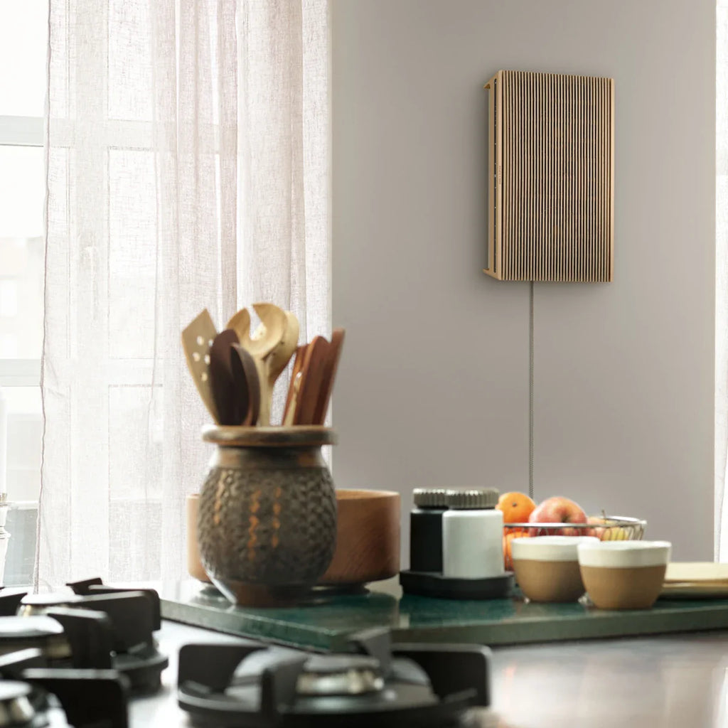 Bang & Olufsen Beosound Level wireless speaker in kitchen with wooden finish, compact and modern design.