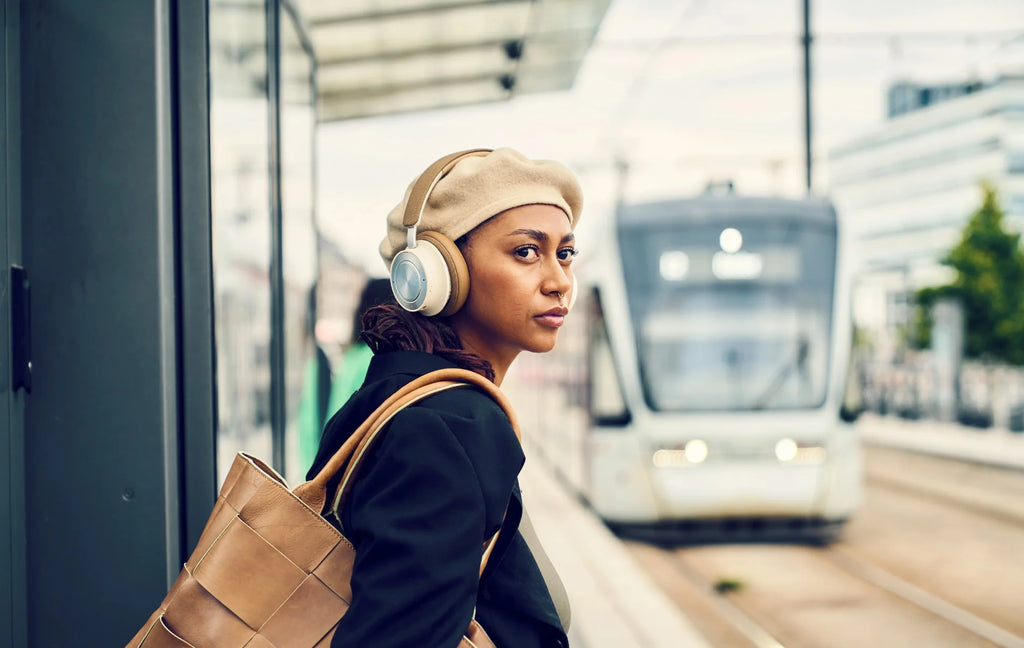 Woman using DALI Dali iO-8 wireless headphones on a tram, showcasing stylish and comfortable in-ear audio experience.