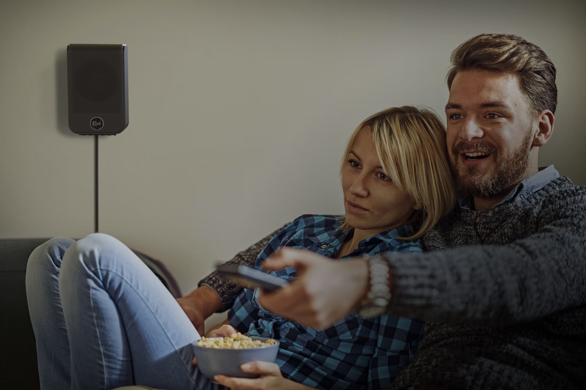 Klipsch Flexus SURR 100 soundbar mounted on wall behind viewers during movie watching, showcasing sleek design and audio setup.
