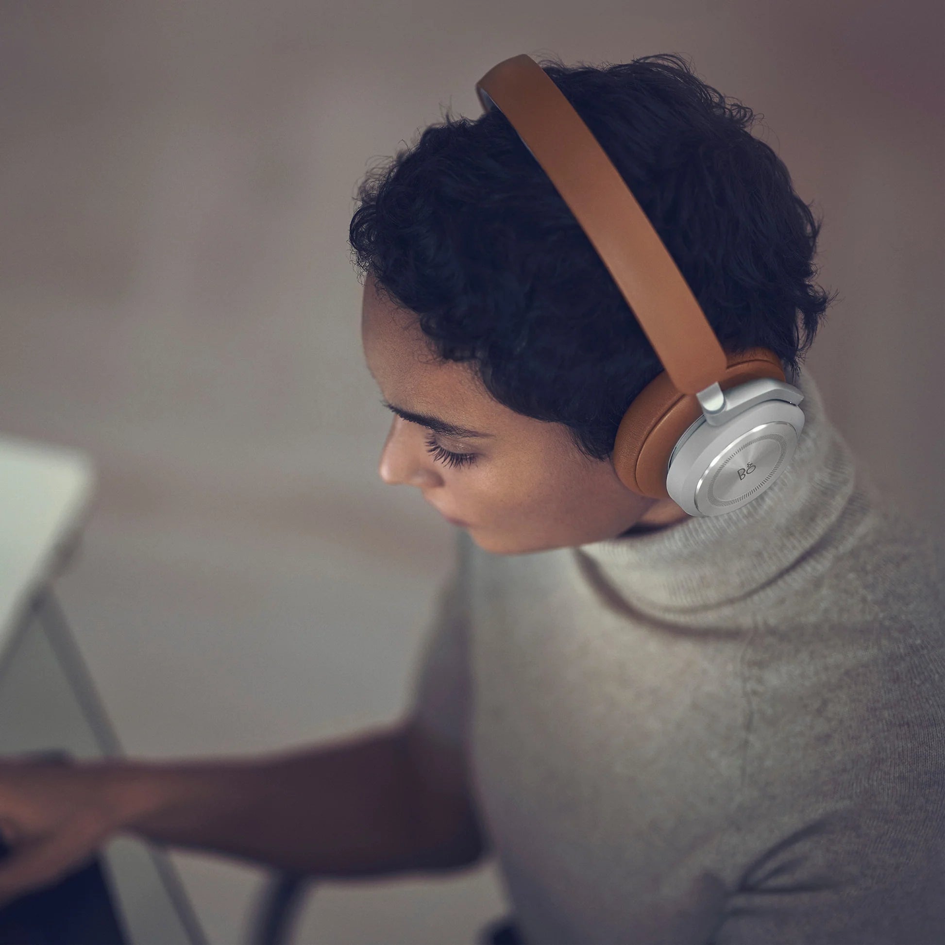 Bang & Olufsen Beoplay HX wireless headphones in timber finish, shown worn in a lifestyle setting with sleek design elements.