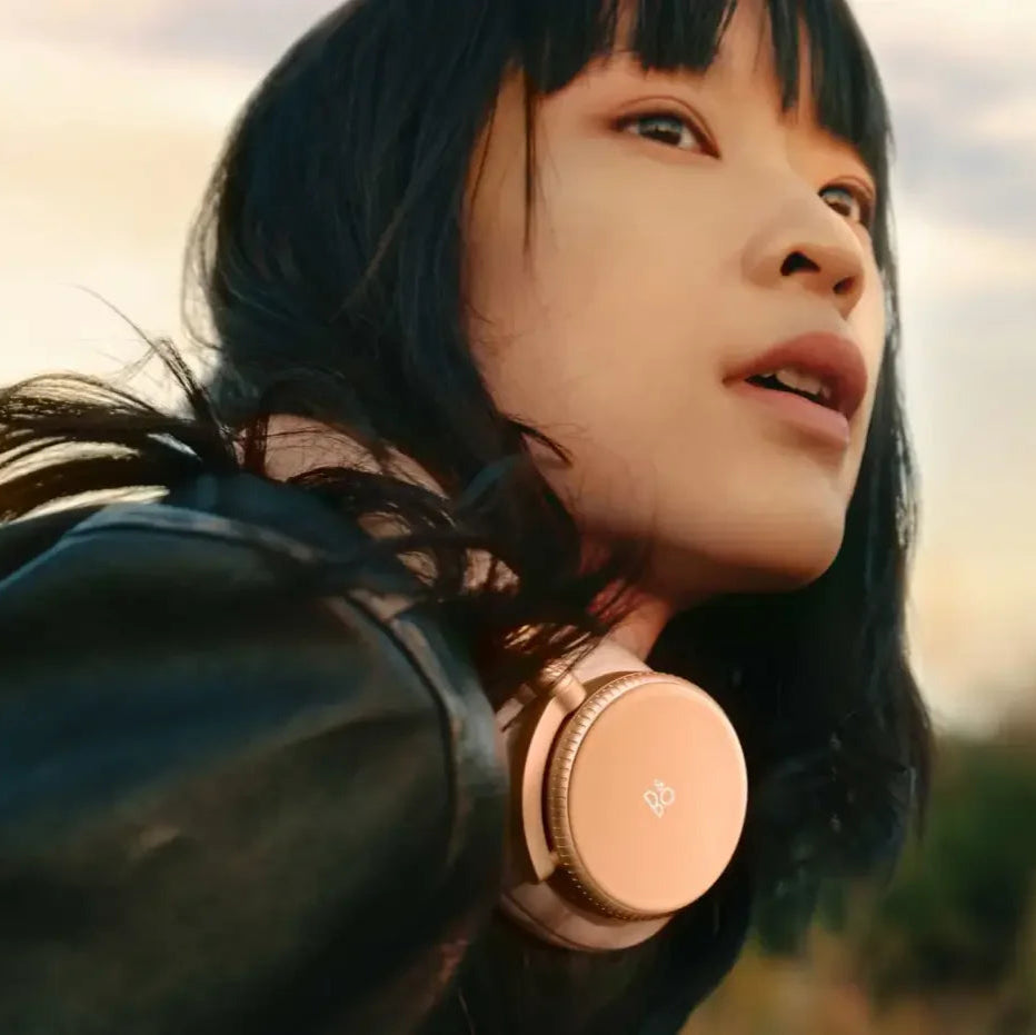 Bang & Olufsen Beoplay H100 wireless headphones worn by a person in a lifestyle setting, showcasing sleek black design and comfortable fit.