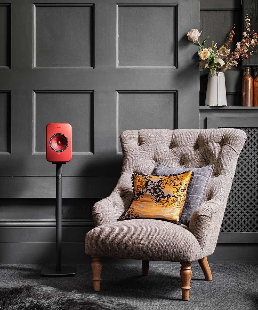 Red KEF S1 speaker stands for KEF LSX speakers, shown with a chair in the background. Durable and stylish speaker support.