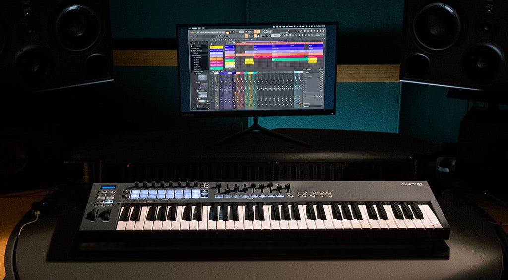 Novation FLkey 61 MIDI keyboard with illuminated pads and control knobs, shown in a music studio setup.