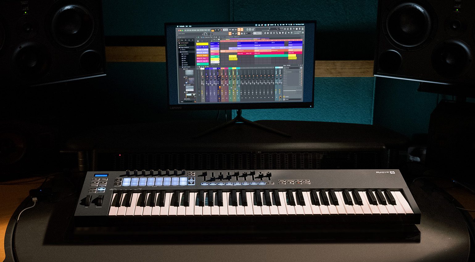 Novation FLkey 61 MIDI keyboard with illuminated pads and control knobs, shown in a music studio setup.