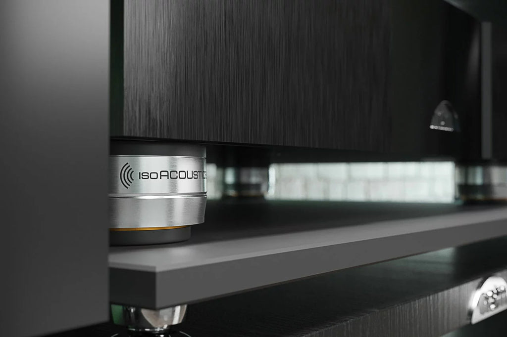 IsoAcoustics Orea Bronze speaker stands on a modern living room floor, supporting audio speakers with a sleek bronze finish.