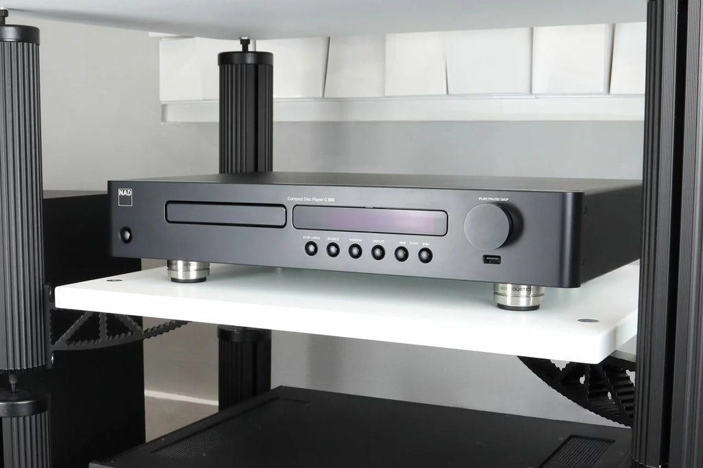 IsoAcoustics Orea Graphite speaker stands shown in a modern living room setting, designed to elevate and stabilize speakers.