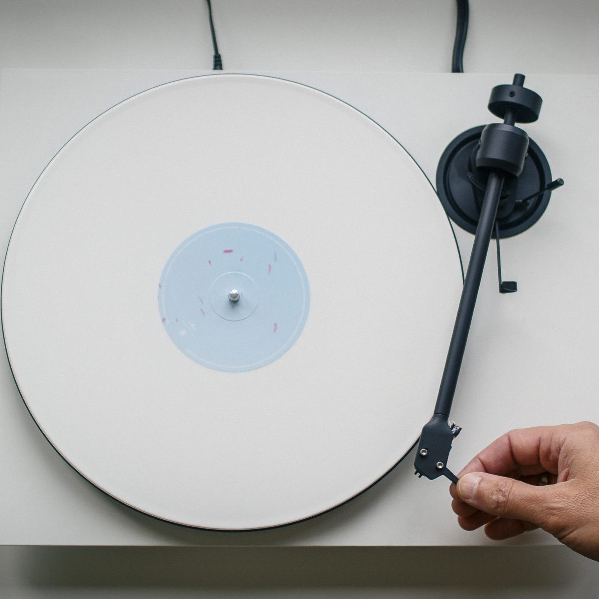 Pro-Ject E1.2 BT Satin White turntable seen from above, a hand guiding the tonearm