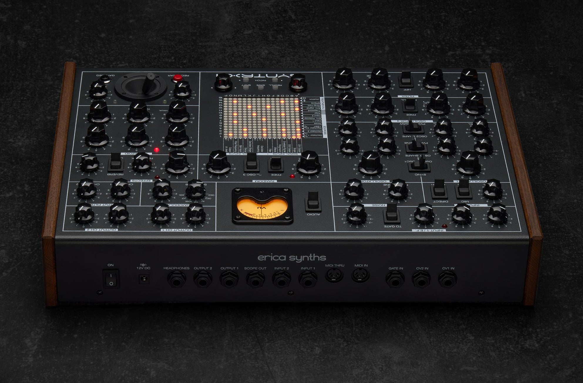 Erica Synths SYNTRX II desktop synthesizer with knobs, buttons, and colorful LED display on a black surface.