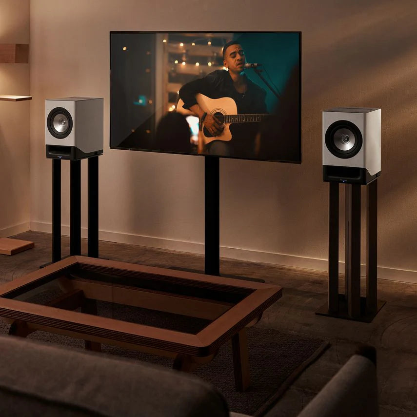 Technics SC-CX700 active bookshelf speakers in gray, shown on a shelf with audio controls and wiring visible.